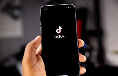 Picture of an iPhone in someone\'s hand with the TikTok homepage on the screen.