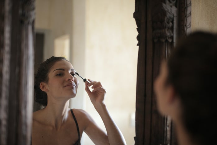 woman staring at her reflection and applying mascara