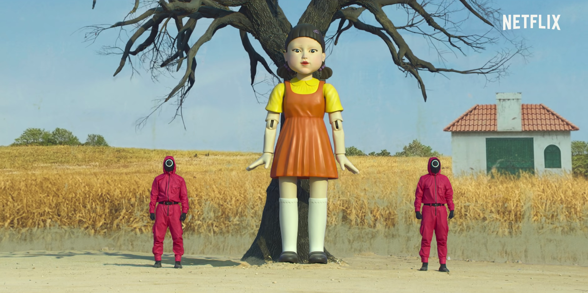 screenshot of a mechanical doll and two workers dressed in red from the Squid Game Official Trailer on YouTube by Netflix