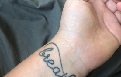 A woman\'s wrist with the cursive word \"breathe\" tattooed on it