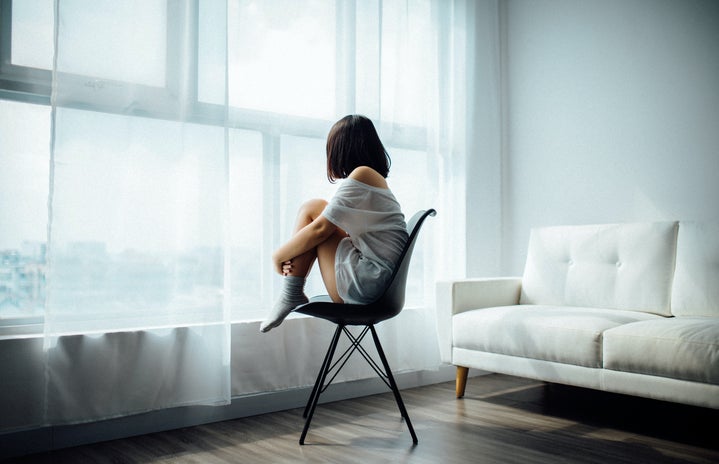 Woman in a white t-shirt and socks sitting on a chair, looking out the window
