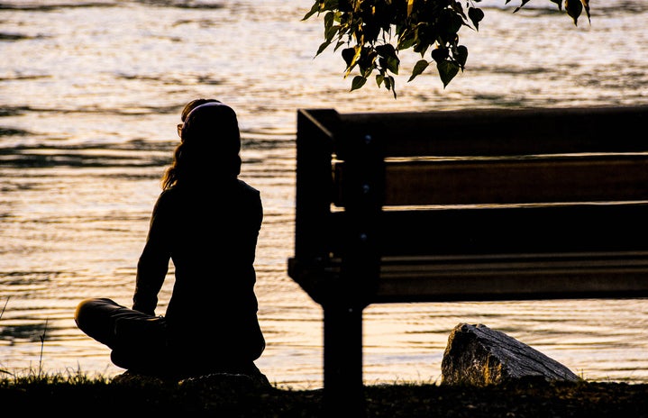 Woman sitting by the river at sunset