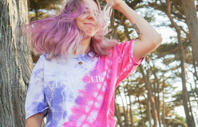 woman with pink hair in blue and pink tie dye shirt in forest