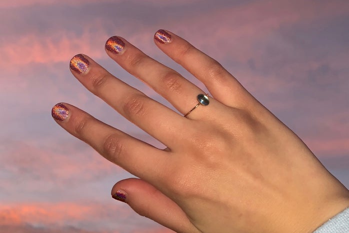 A hand, with sparkly nail polish, in front of a sunset.