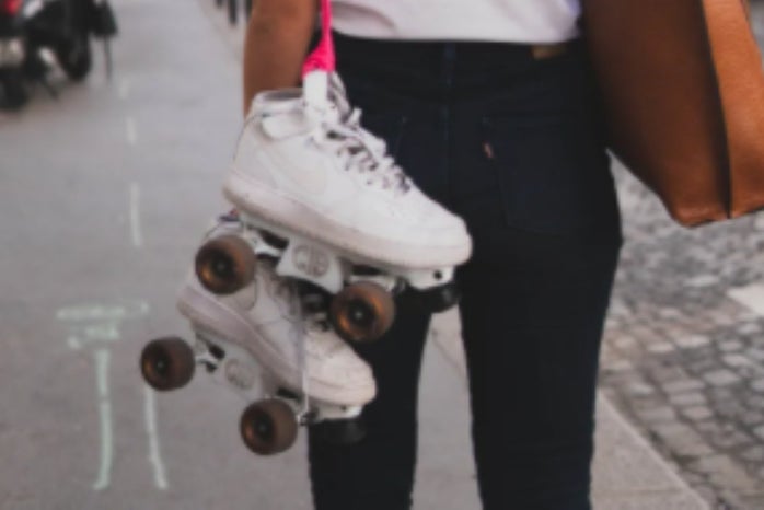 white roller skates hanging off a pink string; black jeans and brown bag.