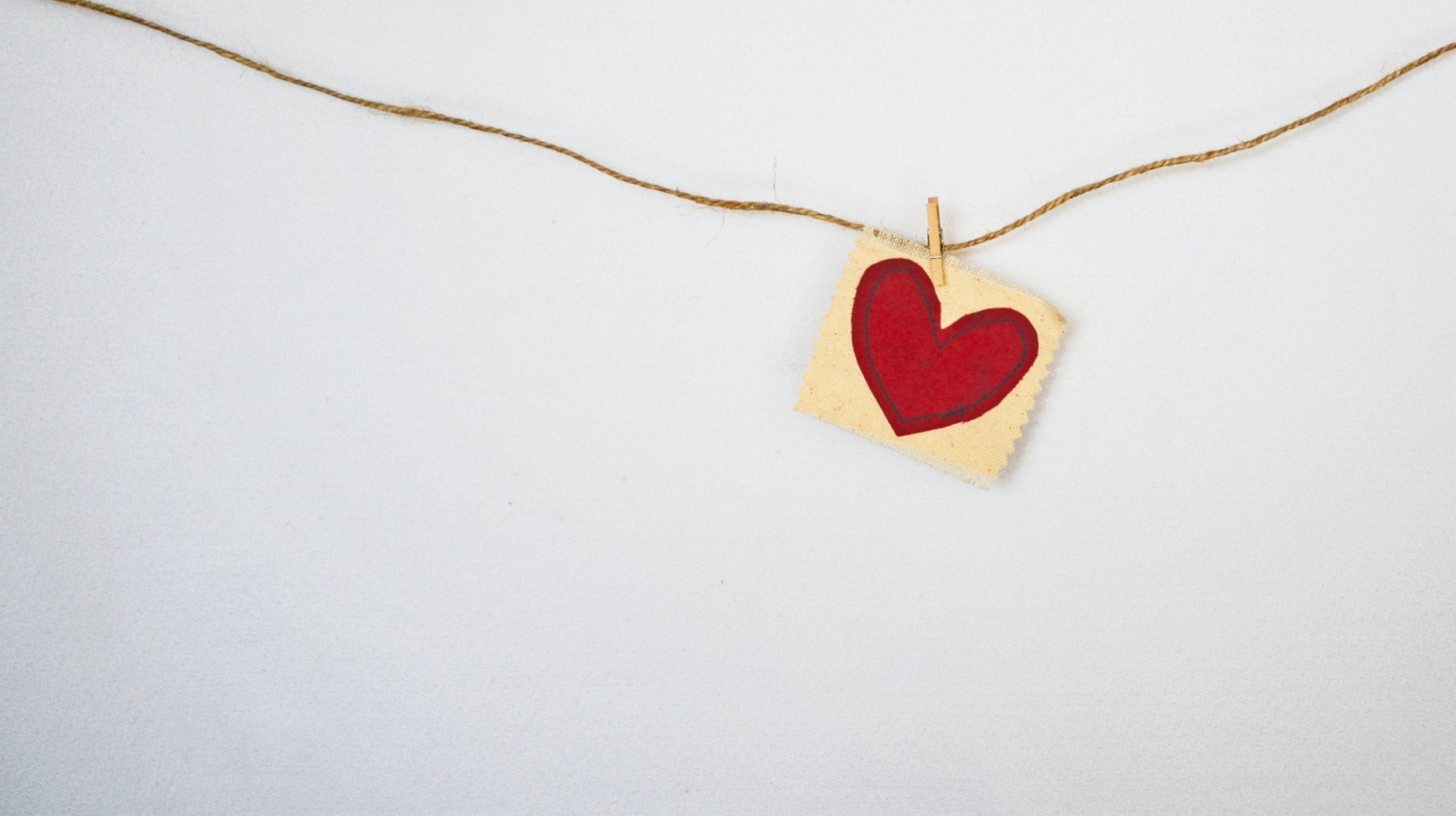 a little read heart attached with a clothespin to a horizontal piece of string against a gray wall