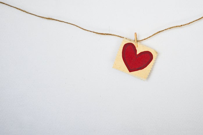 a little read heart attached with a clothespin to a horizontal piece of string against a gray wall