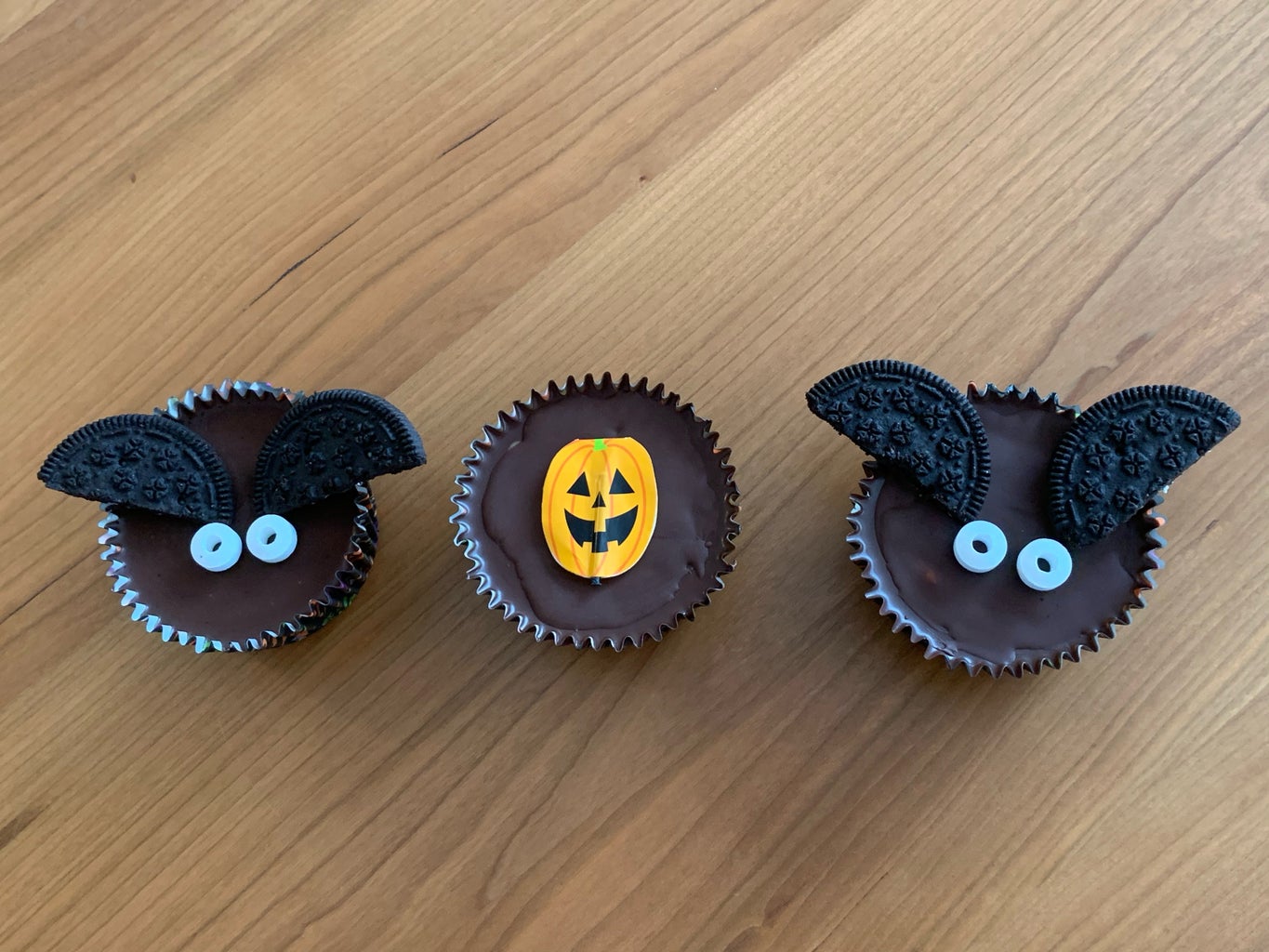 2 bat shaped peanut butter cups and a pumpkin peanut butter cup on a table.