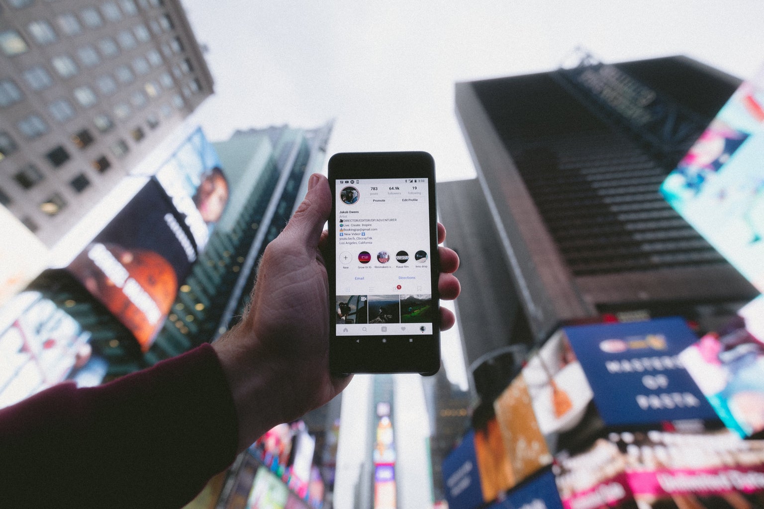 person holding a cell phone up in front of city buildings