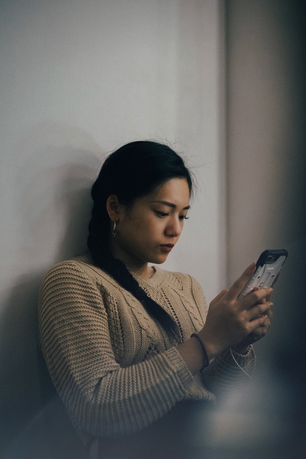 woman leaning back on white wall and using phone