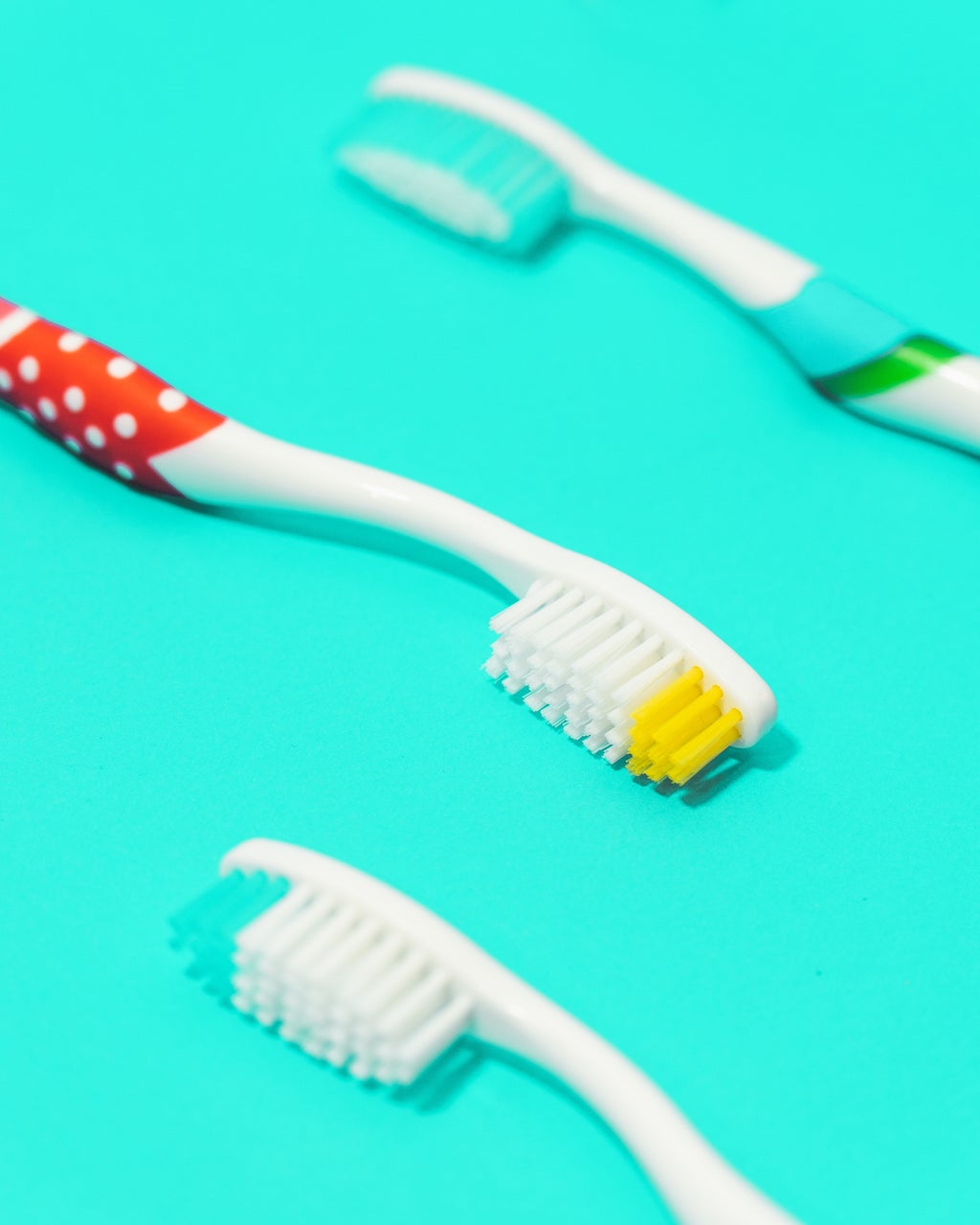 3 toothbrushes with a teal / turquoise background