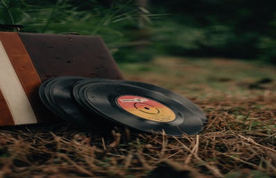 Pile of vintage vinyl discs and aged suitcase on grassy meadow