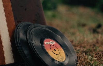 Pile of vintage vinyl discs and aged suitcase on grassy meadow