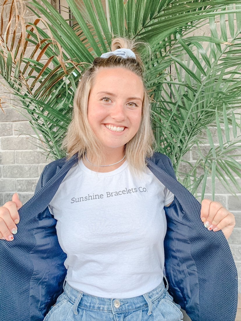 Girl in a white tshirt that says \"Sunshine Bracelets Co.\" (her brand).