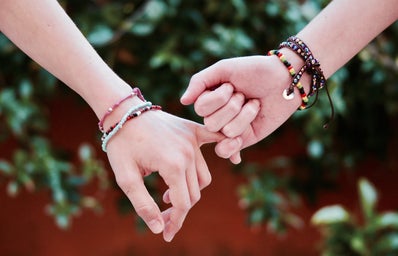 two hands wearing bracelets with pinkies intertwined