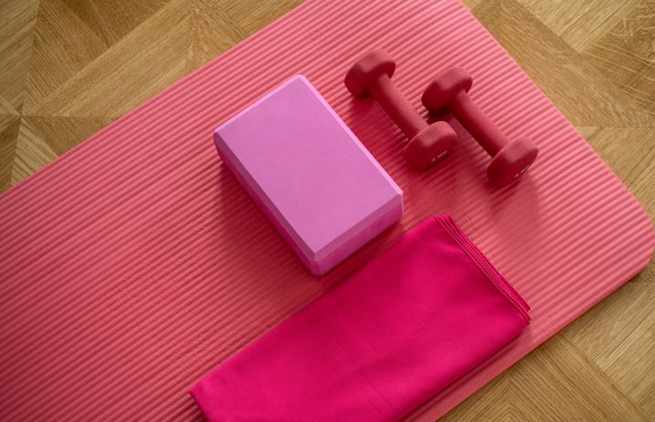 pink yoga mat with two pink weights and other exercise equipment