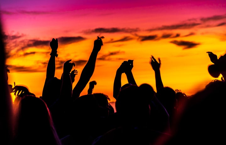 photo of silhouette of people dancing with hands up at sunset