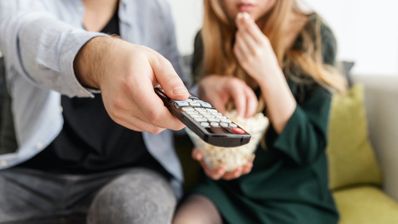 man holding remote, sitting on couch with woman, popcorn
