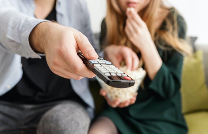 man holding remote, sitting on couch with woman, popcorn