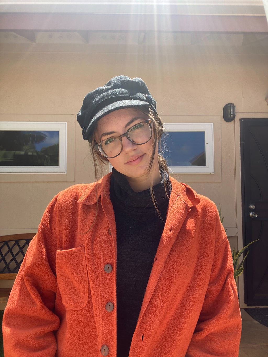 Woman posing, wearing a black hat and orange jacket.