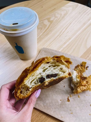 hand holding croissant with coffee on table