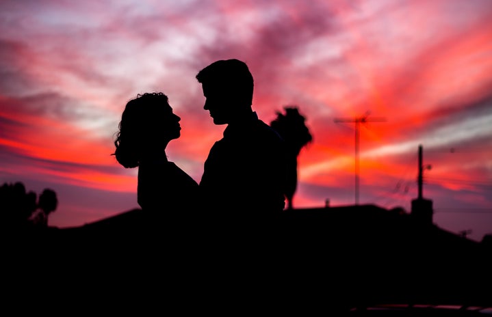 The silhouettes of a man and woman in front of a vivid sunset.