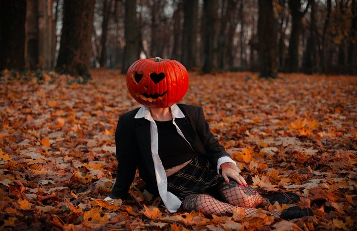 woman with pumpkin head sitting in field