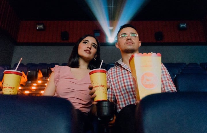 man and woman sitting in theater with popcorn