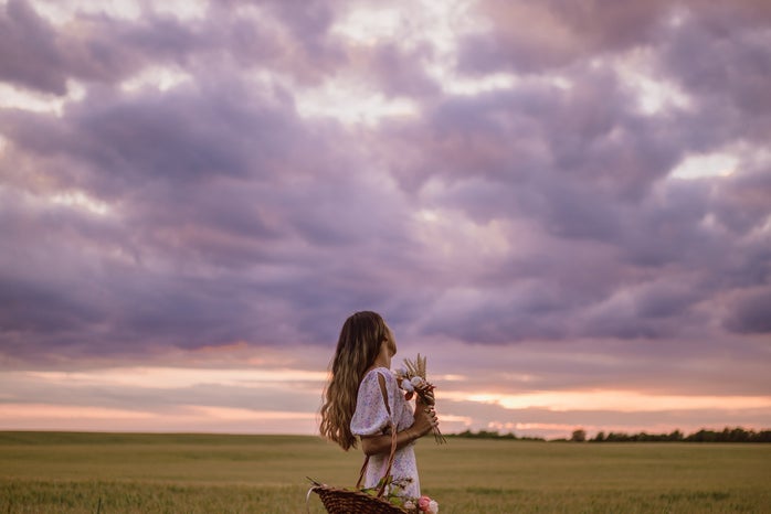 woman with basket and flowers in a field while the sun sets