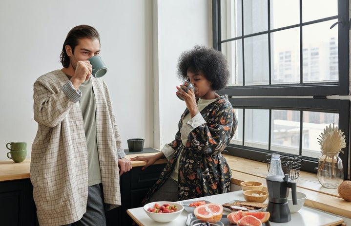 man and woman drinking coffee in kitchen by window