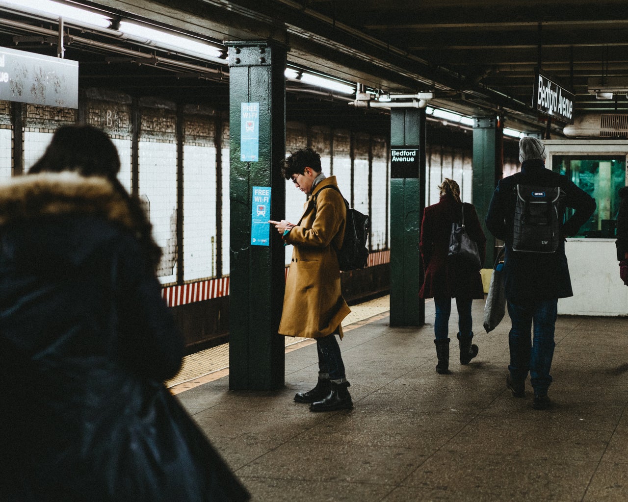 People on their phones, waiting for the next train on a subway platform