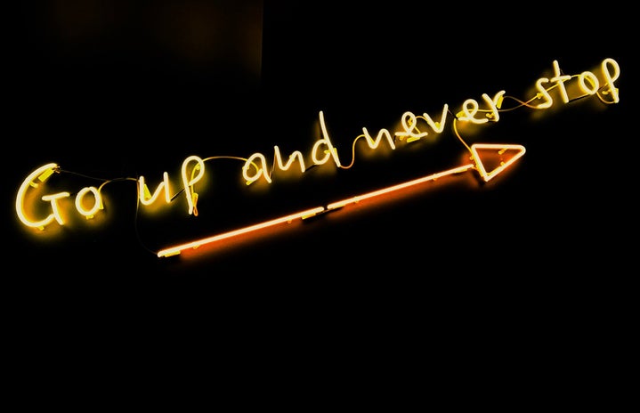 neon quote saying "go up and never stop" on a black background with an arrow underneath the words