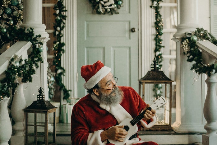 man in santa claus costume holding a ukulele in front of a decorated white house