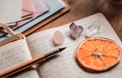 close up photo of a journal with a pen, some crystals, and an orange slice