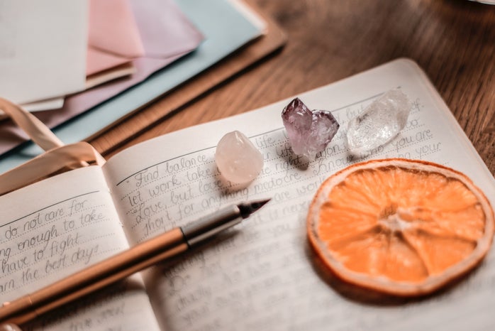 close up photo of a journal with a pen, some crystals, and an orange slice
