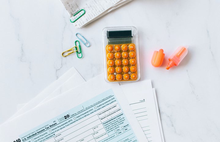A flatlay with a calculator that has orange buttons. A 1040 tax document is below it and paperclips are beside it.