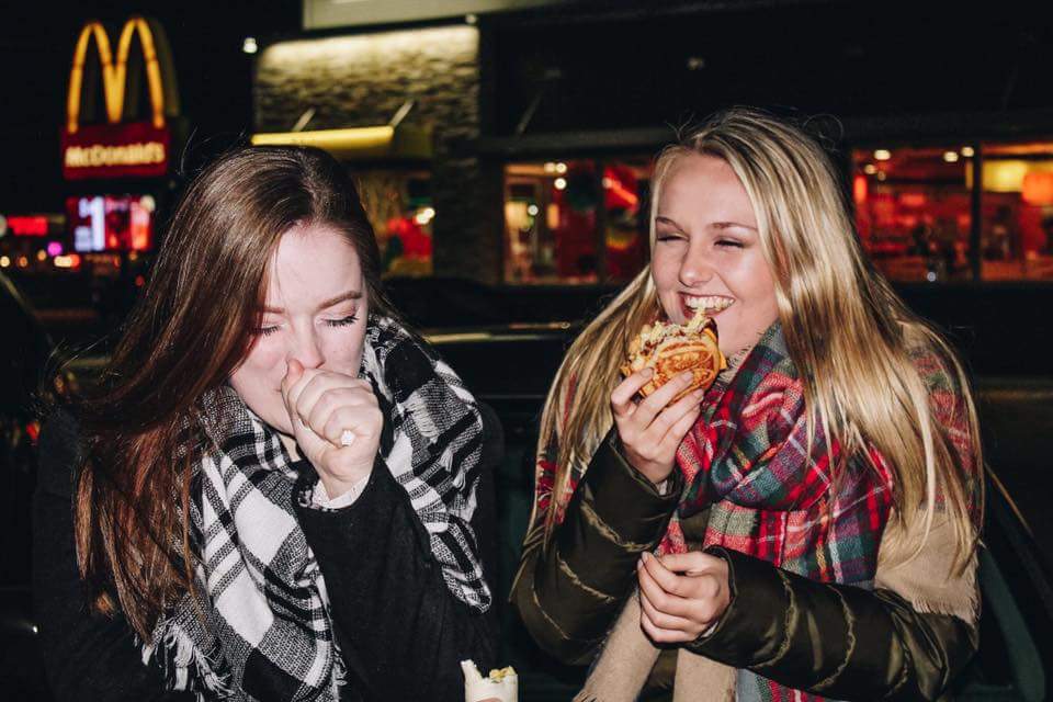 two girls eating on car