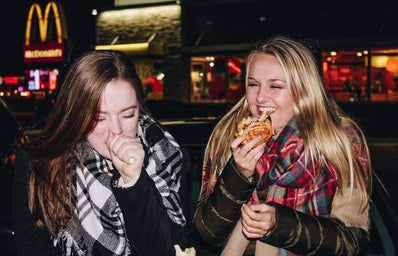 two girls eating on car