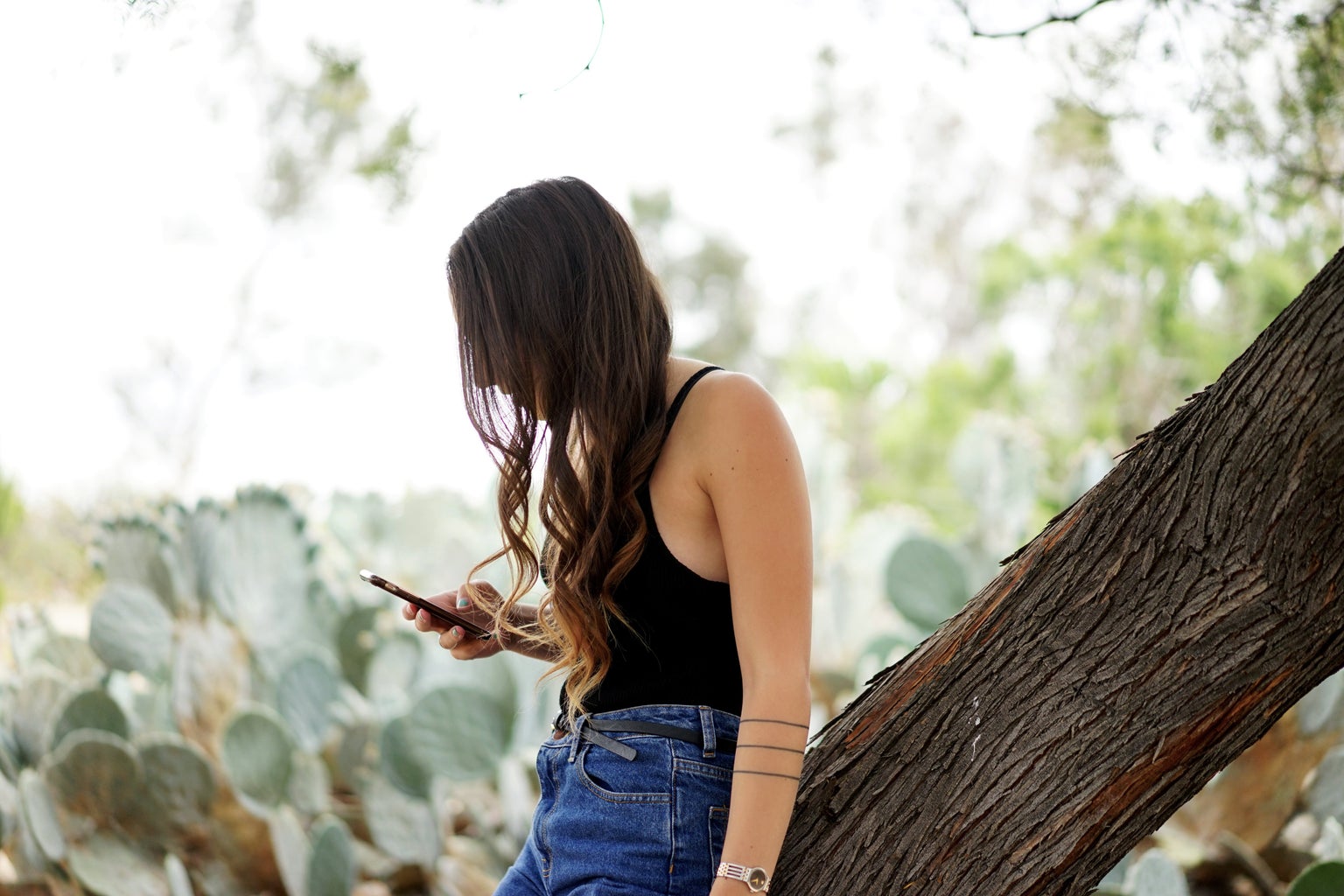 girl scrolling phone high waisted jeans watch curly hair cactus