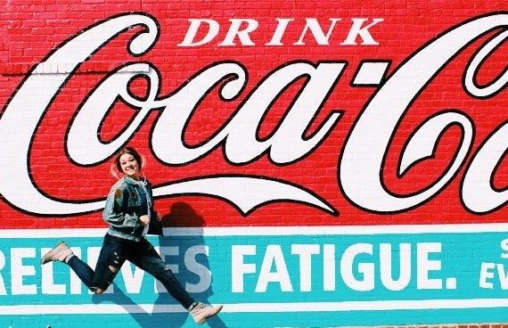 Amelia Kramer-Girl Jumping In Front Of Coca Cola Mural
