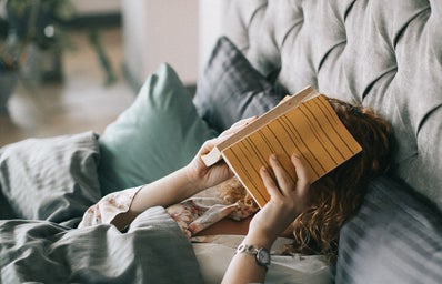 Woman Covering Face With Book On Bed