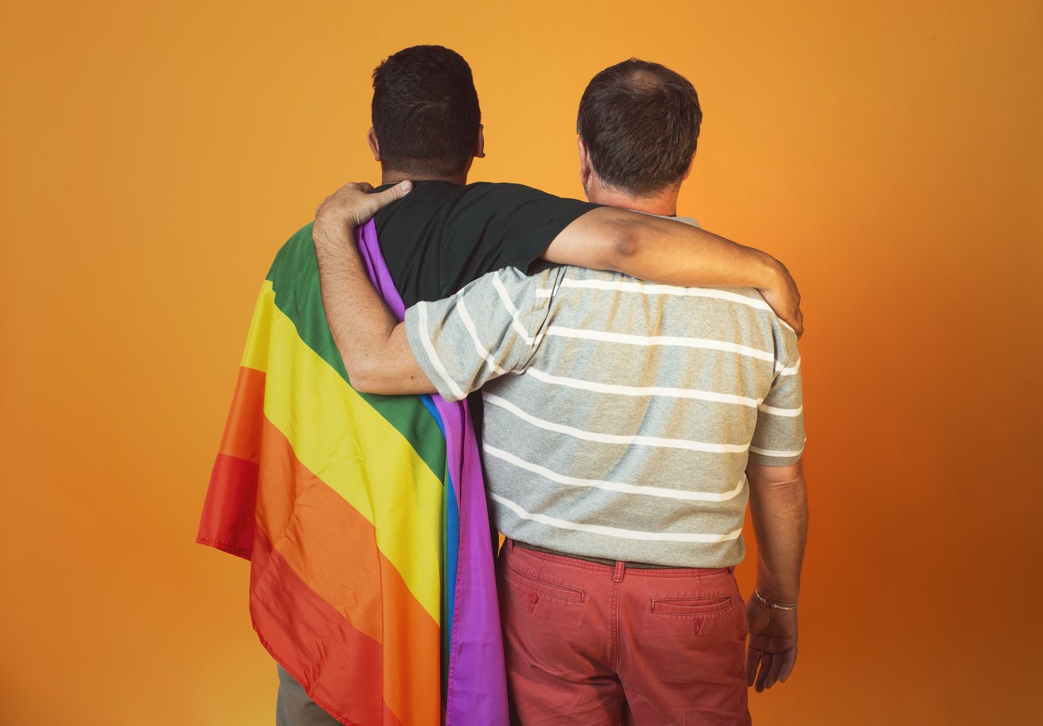 One man with Pride flag, other man hugging him