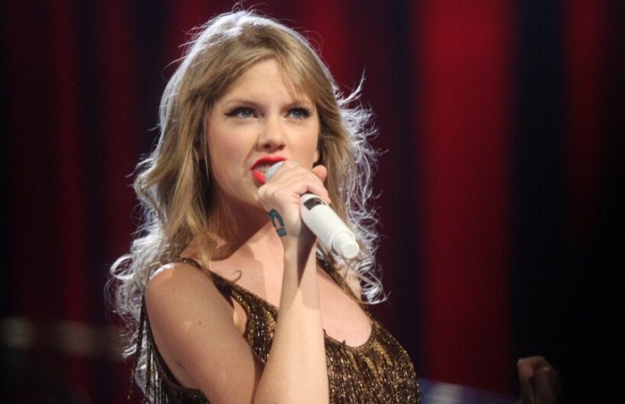 Taylor Swift on stage singing in a gold sequin dress