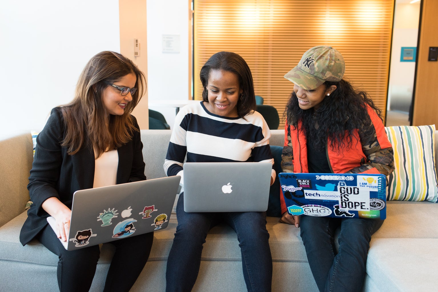 three women sitting on a couch with laptops