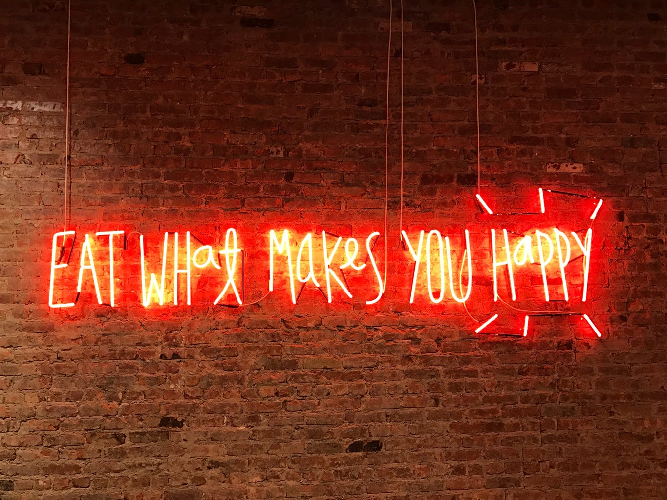 eat what makes you happy neon sign on brick wall