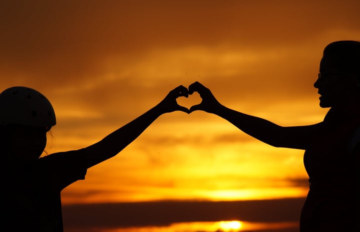 Two people holding hands in heart shape during sunset