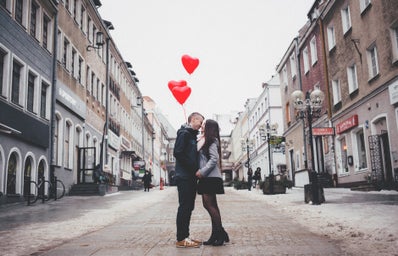 couple kissing in the street with heart balloons in the background