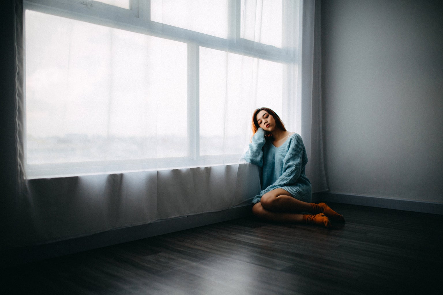 sad girl in blue sweater near window