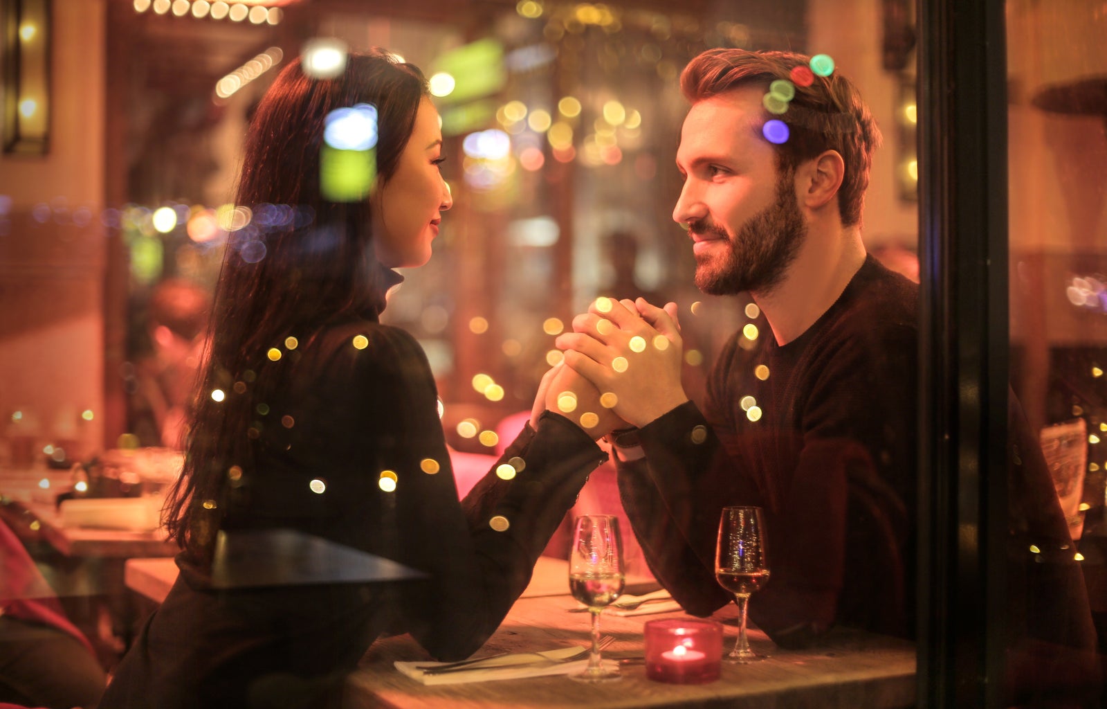 couple seen holding hands through the window at a table with two glasses of wine on the table