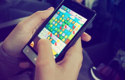 A smartphone user holds their phone, playing a game that looks like Candy Crush